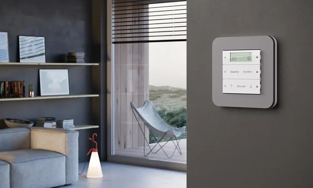 Gira Tastsensor mit Anzeige an einer grauen Wand, dahinter ein Wohnraum